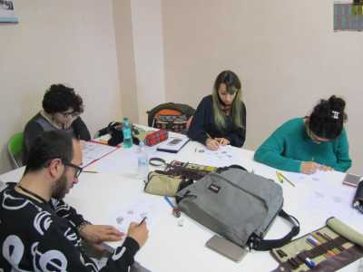 Intorno a un tavolo seguiamo i ragazzi disegnare mentre ascoltano la lezione del docente